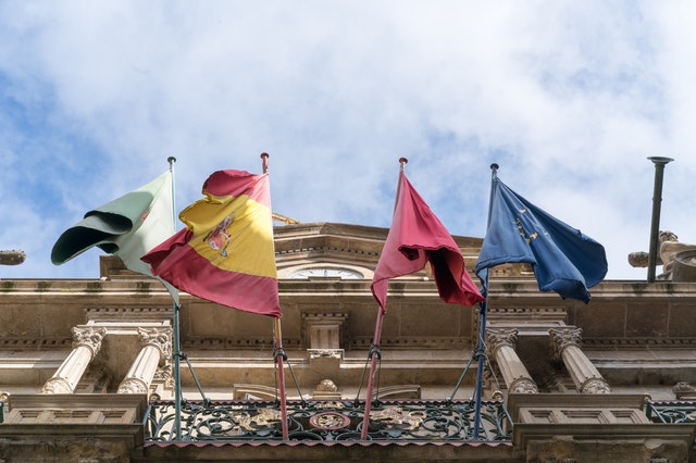 Flags waving on old ornate city building on fine day. ©Pexels/ArtHouse Studio - pexels.com. All rights reserved